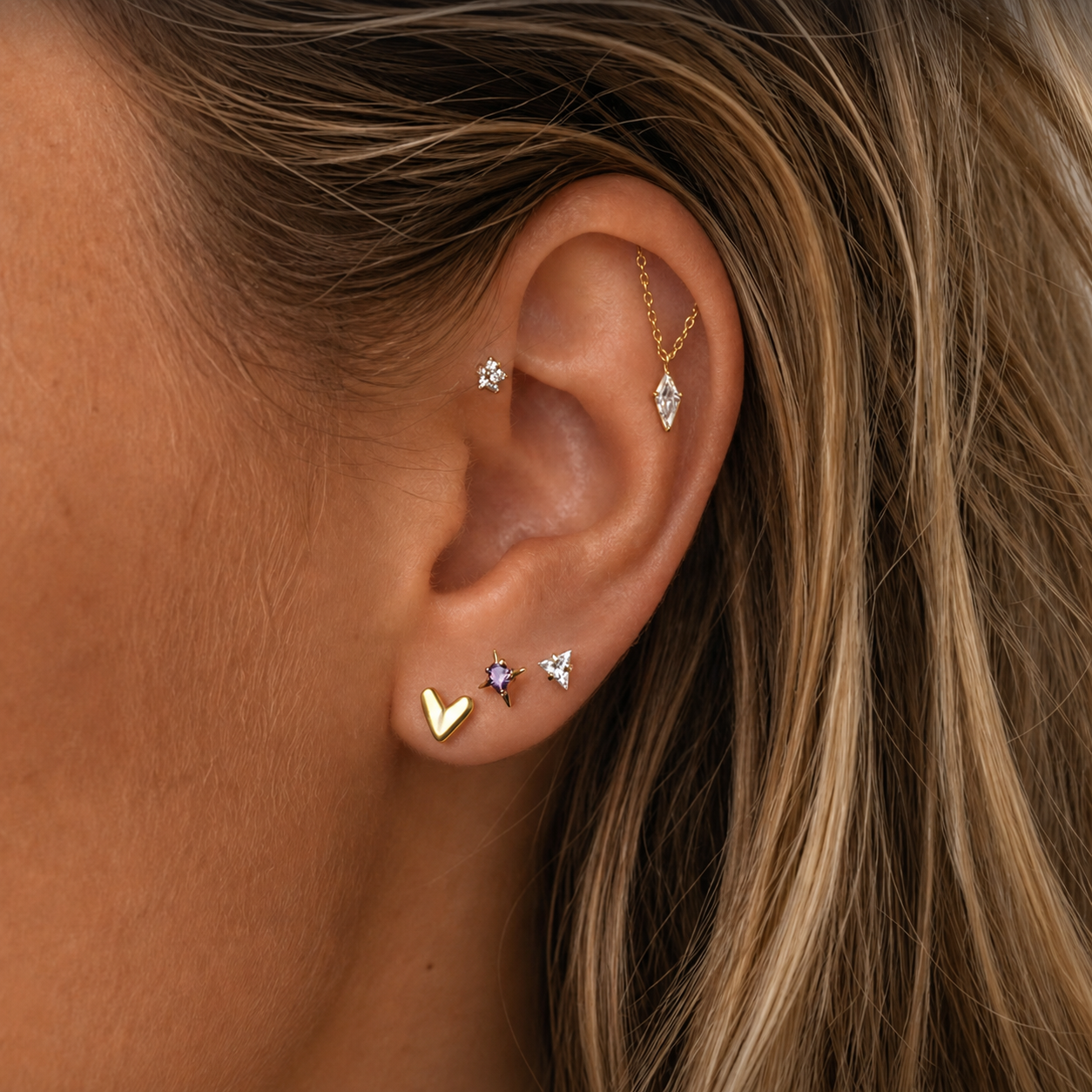 close up van een oor met gouden sieraden en blond haar